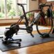High-density foam bike trainer mat laid flat on a hardwood floor beneath a stationary indoor cycling trainer