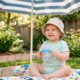 Toddler sitting in shade wearing a sun hat drinking water from a sippy cup